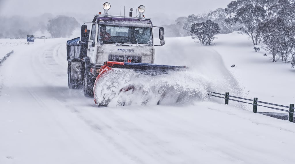 A powerful snow plow truck clearing a snow-covered road in a serene winter landscape.